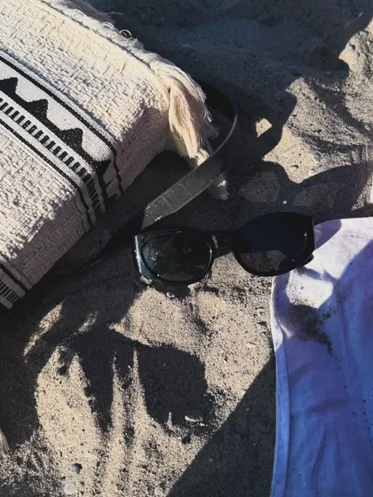 An aesthetic shot of my beach essentials: sunglasses and a tote bag on the sand.