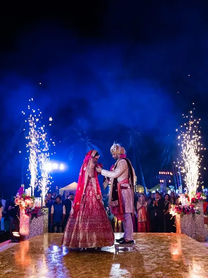 A dramatic varmala moment at a beach wedding, with the couple framed by pyrotechnics against the night sky. This showcases our ability to create spectacular moments in any setting.