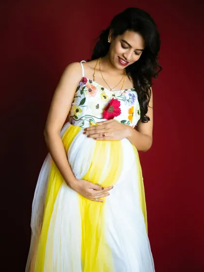 A close-up of the summer-colored gown, focusing on the expecting mother's happy expression as she holds her baby bump.
