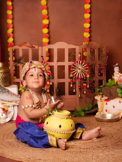 A sweet baby boy dressed as Kanha, sitting with his pot of butter in our traditional Janmashtami setup.