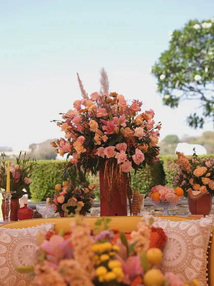 A grand floral centerpiece in warm tones stands behind a yellow sofa, creating a stunning focal point in the garden lounge.