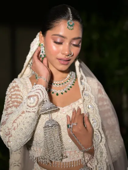 A serene and elegant pose. The bride looks like a vision in her white and pink lehenga, with flawless makeup and stunning jewelry.