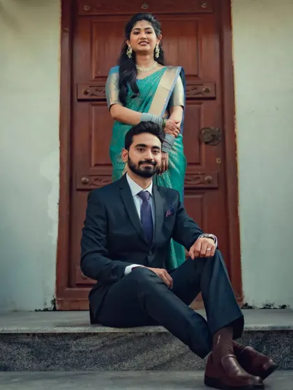 A stylish portrait of a couple, the groom seated while his partner stands behind him, both looking confident and happy.