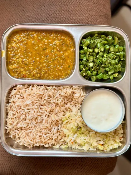 This simple and healthy thali includes brown rice, dal, sautéed green beans, and a side of curd and cabbage palya.