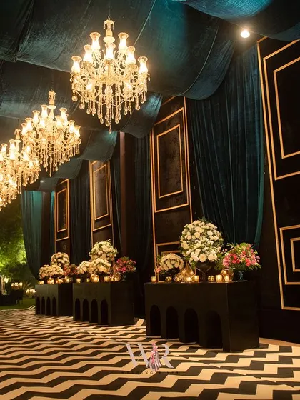 A different angle of the dramatic entrance, showing the long row of chandeliers leading the eye towards the main event space. The floral consoles on either side add softness and color.
