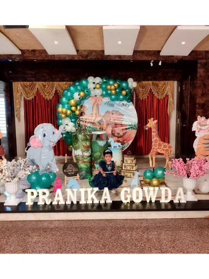 A grand jungle-themed stage decoration for a first birthday, featuring large animal cutouts and a circular backdrop with the birthday girl's photo.