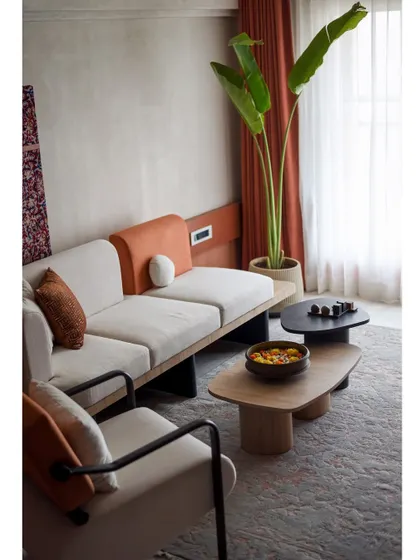 The living room of 'A Den' is filled with earthy tones and natural materials. The custom sofa and coffee tables create a comfortable and inviting seating area.