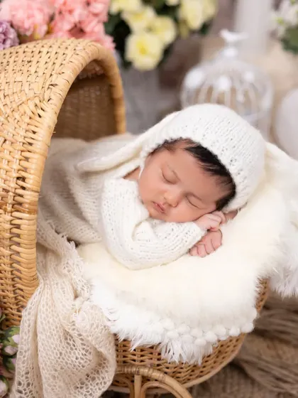 A close-up of our sleeping bunny theme, this time in a charming rattan bassinet. The soft, warm lighting emphasizes the baby's peaceful sleep and the cozy knit texture of the outfit.