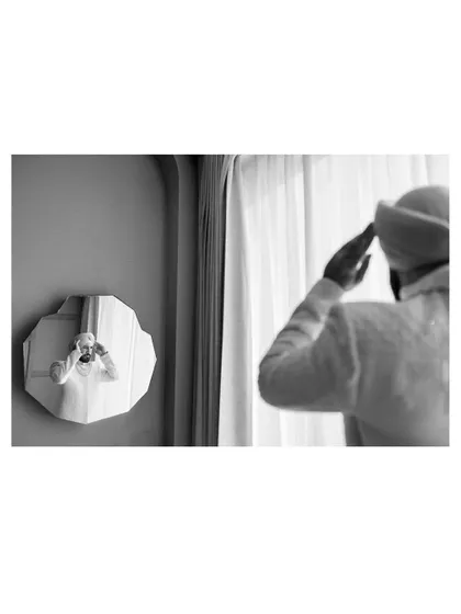 An artistic black and white shot of the groom adjusting his turban while looking in a uniquely shaped mirror.