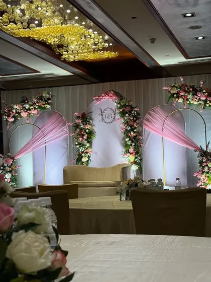 An elegant engagement stage with pastel pink drapes and floral arrangements. The couple's monogram in the center adds a personalized touch.