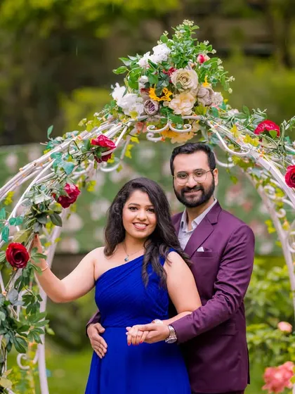 A happy couple portrait framed by a beautiful floral arch. The vibrant blue dress and the genuine smiles make this a simple yet heartwarming shot from their pre-wedding session in a Bangalore garden.