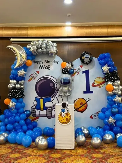 A full view of another space-themed party for Nick's first birthday, with a large backdrop, astronaut foil balloons, and a rocket-ship motif.