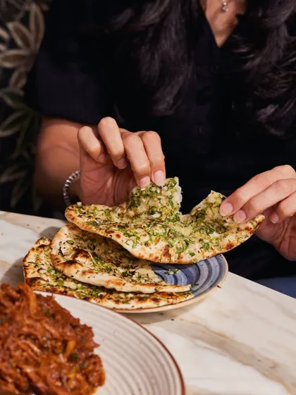 A hand tears into a piece of our Chilli Garlic Naan. It's soft, chewy, and packed with flavour, ideal for scooping up rich curries.