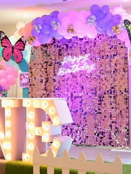 The main stage for a butterfly-themed first birthday, featuring a pink sequin wall, "ONE" marquee letters, and a rainbow-colored balloon arch.