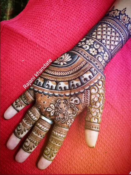 A close-up of a hand with a symmetrical design. This pattern features a beautiful arc of elephants, a central floral mandala, and intricate filler work, all done with exceptional neatness.