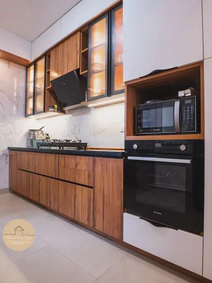 A kitchen should be both beautiful and functional. This contemporary kitchen at a Godrej Air Hoodi project showcases a seamless blend of warm wooden textures and glossy white laminate. The fluted glass cabinets with interior lighting add a touch of sophistication while providing practical storage.