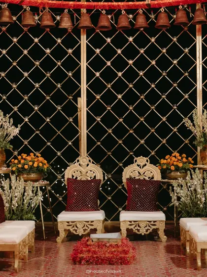 The bride and groom's ornate seating inside the bell mandap, framed by a golden lattice and hanging temple bells, creating an intimate and sacred space for the couple.