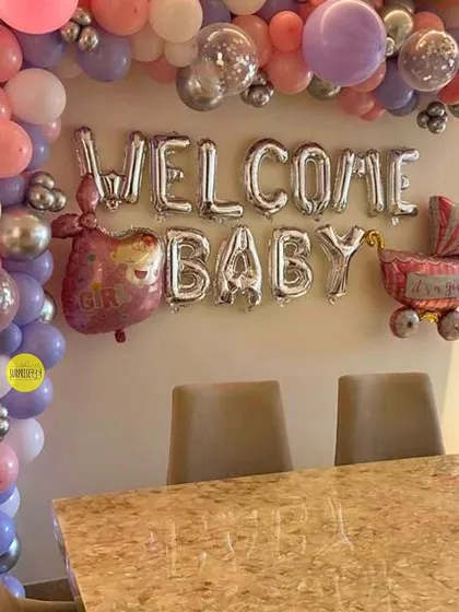 A classic "Welcome Baby" setup with silver foil balloons and a pink and purple balloon arch. This is a simple yet beautiful way to decorate the dining area for a homecoming meal.