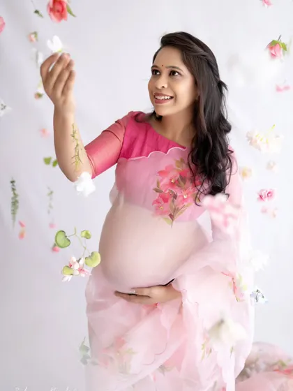 A playful and happy solo shot. The mom-to-be interacts with the hanging flowers, her smile capturing the lighthearted and magical side of her pregnancy journey.