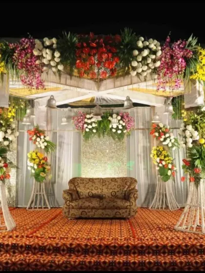 A traditional stage setup for a wedding reception, featuring a colorful explosion of flowers on a raised platform with a classic sofa for seating.