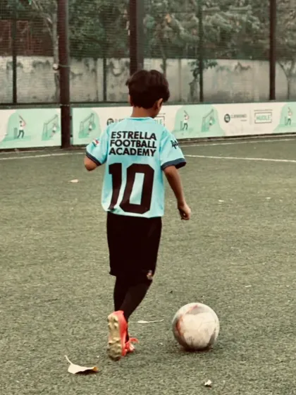 A player dribbling with purpose, showcasing the confidence and skill developed through our consistent training programs. The back of the jersey proudly displays the academy name.