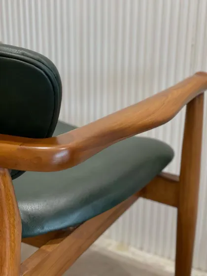 The "Catwalk" chair, featuring a sleek teak wood frame and a deep green leatherette seat. This piece perfectly blends warm, natural wood with a modern, casual aesthetic.