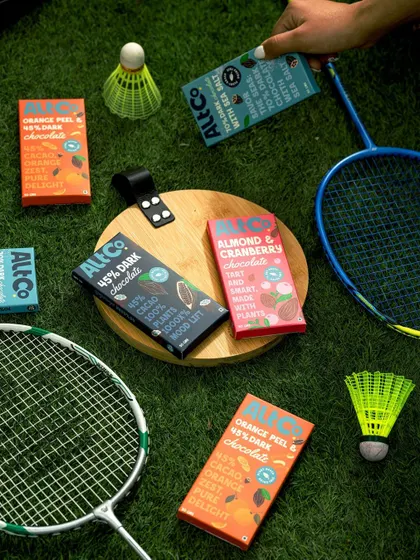 A playful flat lay of Alt Co. chocolates and badminton gear on a grassy lawn. This composition associates the brand with an active, fun, and outdoor lifestyle.