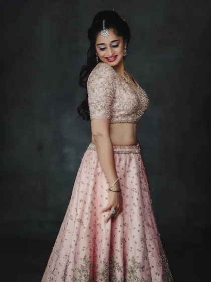 An elegant studio portrait in a soft pink lehenga. The simple, dark background makes the delicate embroidery and the model's happy expression the main focus of the image.