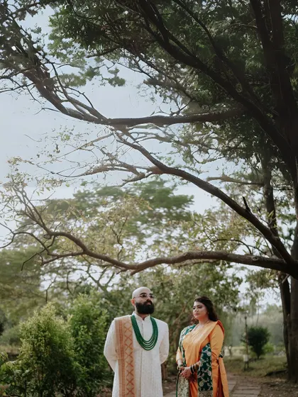 A wide-angle portrait that establishes the scene. The couple stands under a large tree, creating a sense of scale and capturing the beauty of the natural surroundings.