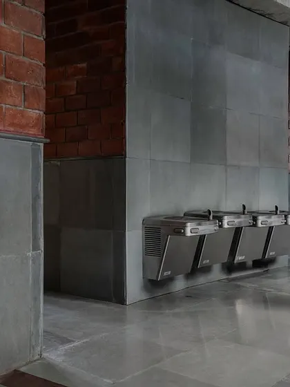 A functional common area within the school, showcasing the honest materiality of exposed brick and grey Kota stone. Even utilitarian spaces like this water fountain area are designed with durability and a cohesive aesthetic in mind.