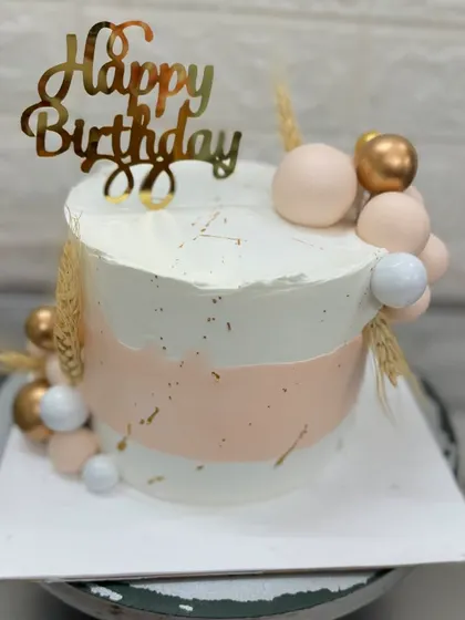 A stylish and modern birthday cake with a soft pink and white watercolor effect. The golden spheres and wheat stalks add a unique and artistic touch to this custom design.