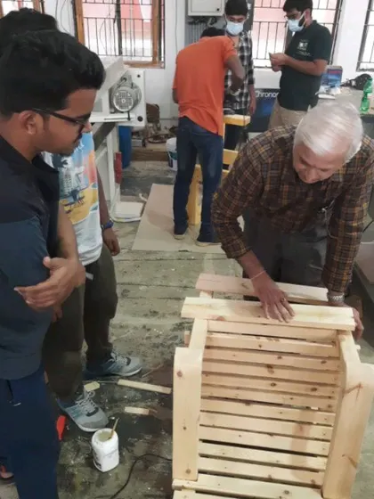 An instructor provides hands-on assistance to students assembling a chair, ensuring they understand the nuances of fitting complex joints.