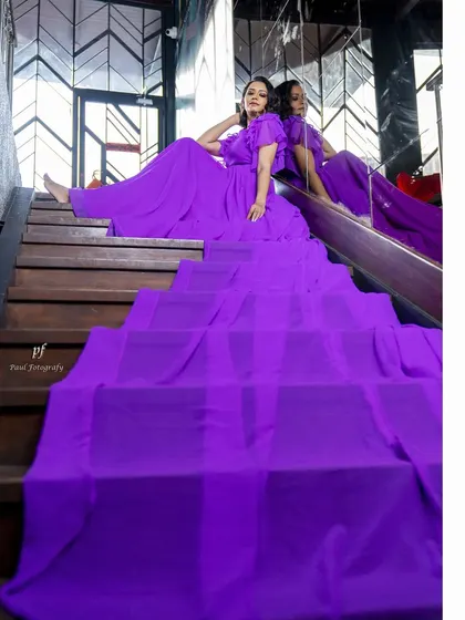 A dramatic, flowing gown in a rich purple hue, designed to create movement and elegance. The long, sweeping train and ruffled sleeves make it a perfect piece for a photoshoot or a grand entrance.