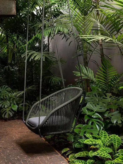 A different angle of a woven swing chair surrounded by a variety of large-leafed plants and palms. This demonstrates how we use dense planting to create a sense of enclosure and privacy.