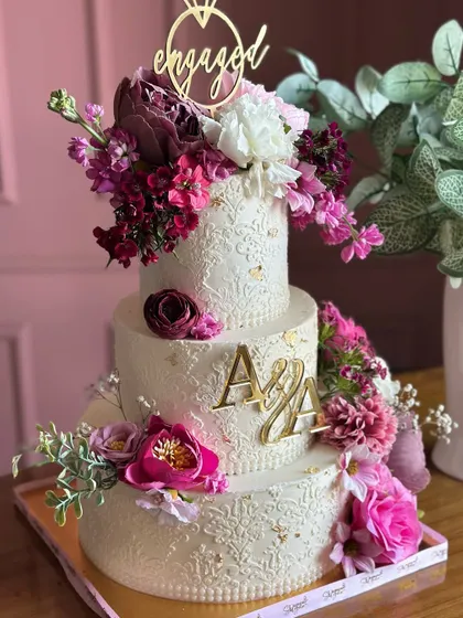 This exquisite three-tiered engagement cake features a pristine white finish with delicate, hand-piped details. A cascade of exotic, vibrant flowers adds a perfect contrast, symbolizing a love that is both pure and full of life.