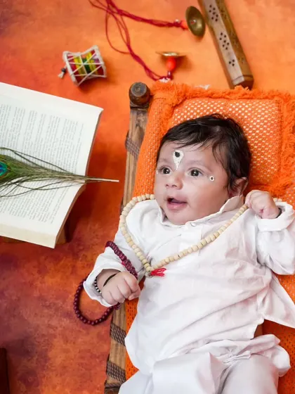 Looking up with wonder, this baby boy is styled perfectly for the Vitthal theme, with a peacock feather and holy book adding to the spiritual feel.