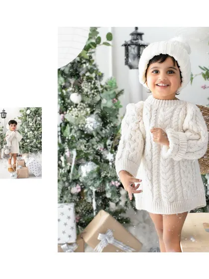 A big, bright smile for the holiday season. This little one's joy is infectious in her cozy white outfit against the snowy Christmas tree backdrop.