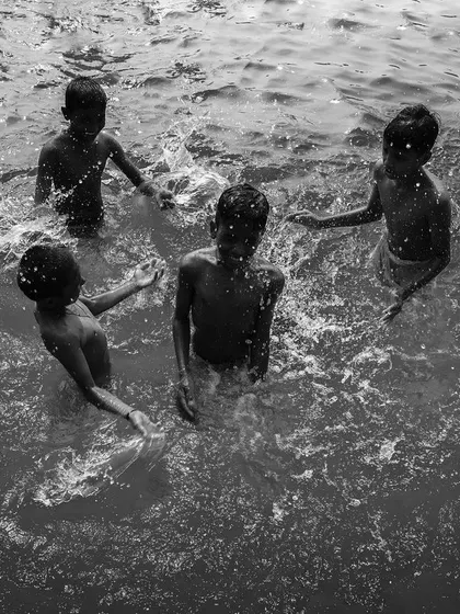 Four boys play together in the water, their splashing creating a circle of friendship and joy. A timeless black and white moment of childhood.
