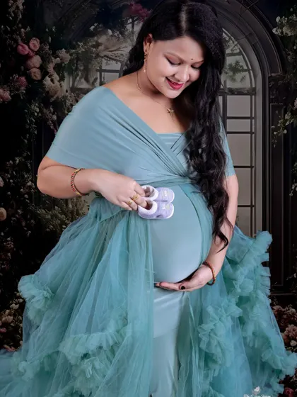 A sweet and tender solo portrait. The mom-to-be looks down at the tiny baby shoes she holds against her bump, a classic and emotional maternity pose.
