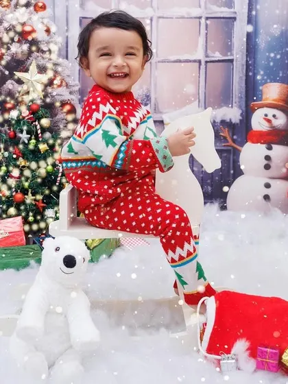 A joyful toddler in a Christmas sweater rides a rocking horse in a snowy, magical setting.