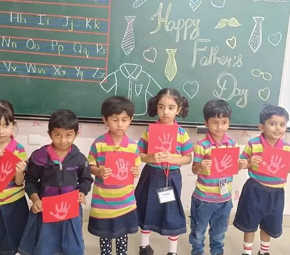 A group of students in front of the "Happy Father's Day" blackboard drawing, showcasing their handmade cards.
