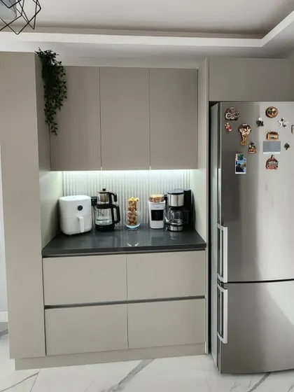 A compact and modern crockery or pantry unit in Pamposh Enclave. The design features handleless cabinets, a dark countertop for appliances, and a fluted backsplash with task lighting.