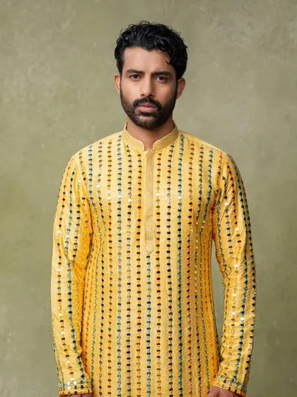 A classic portrait for a men's festive wear collection. The lighting highlights the sequin details on the bright yellow kurta.
