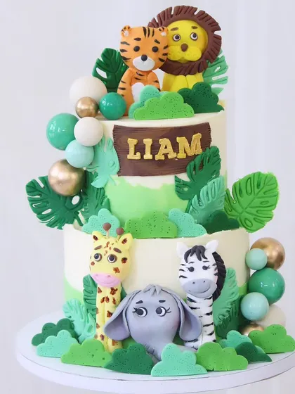 It's a jungle out there! This adorable two-tiered jungle cake is filled with friendly fondant animals, including a tiger, lion, giraffe, and elephant, all nestled among lush green leaves.