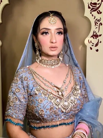 A close-up of the ethereal powder blue look. The focus is on luminous skin, soft pink blush, and sparkling eyes, framed by a delicate blue dupatta.
