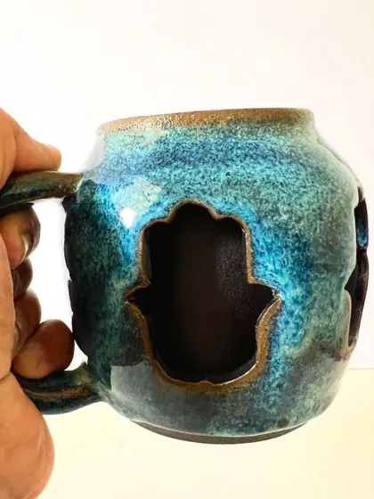 Holding the Hamsa mug, you can see how the cut-outs create a beautiful contrast between the outer and inner walls.