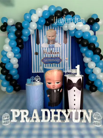 A classic Boss Baby themed party. The setup includes a blue and white striped backdrop, a balloon arch, and themed pedestals, including one designed like a tuxedo.