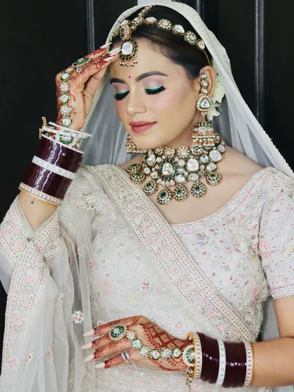 A close-up of a bride in a white lehenga. The makeup features a striking green and pink eyeshadow look, showing how to play with color for a modern bridal style.