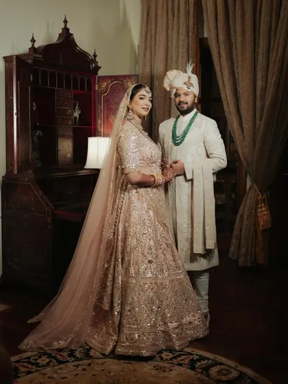 A formal portrait of Sanskriti and Rahul at Rambagh Palace, standing in a room filled with antique furniture and heritage decor.