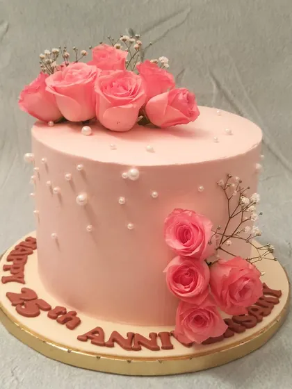 We commemorate a 25th anniversary with timeless elegance. This soft pink cake is adorned with a bouquet of fresh pink roses, sprigs of baby's breath, and scattered pearls, creating a romantic and classic design to celebrate a silver jubilee.